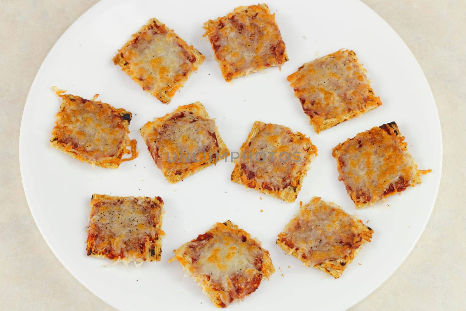 Ten square, broiled mini pizza snacks on a white plate.