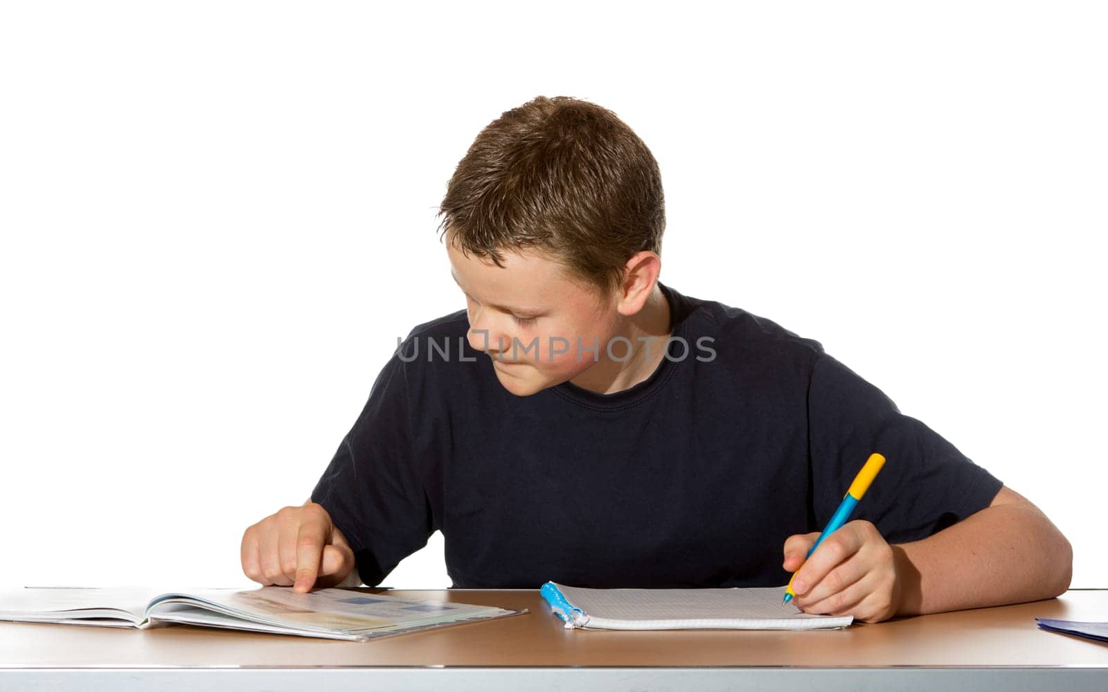 Teenage boy concentrating on his studies as he makes notes in a book from the information he is researching in his textbook