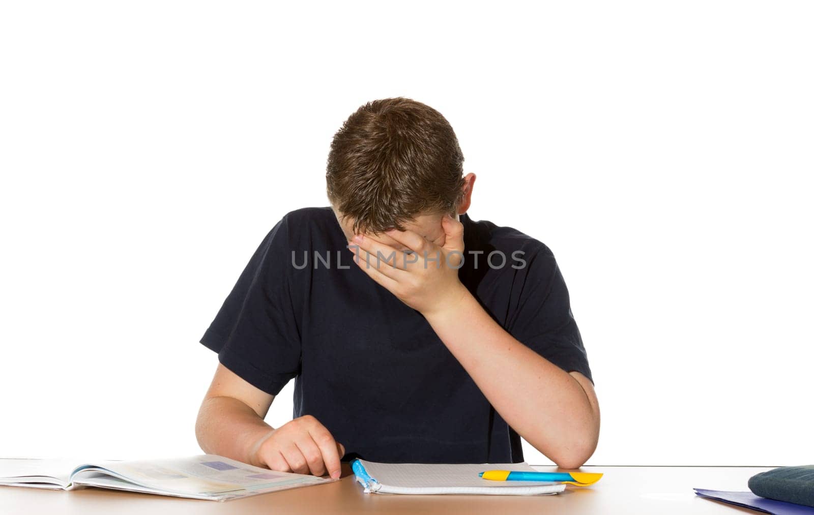 Young teenage boy overwhelmed by his studies sits at his desk with his head in his hand and his textbooks open in front of him