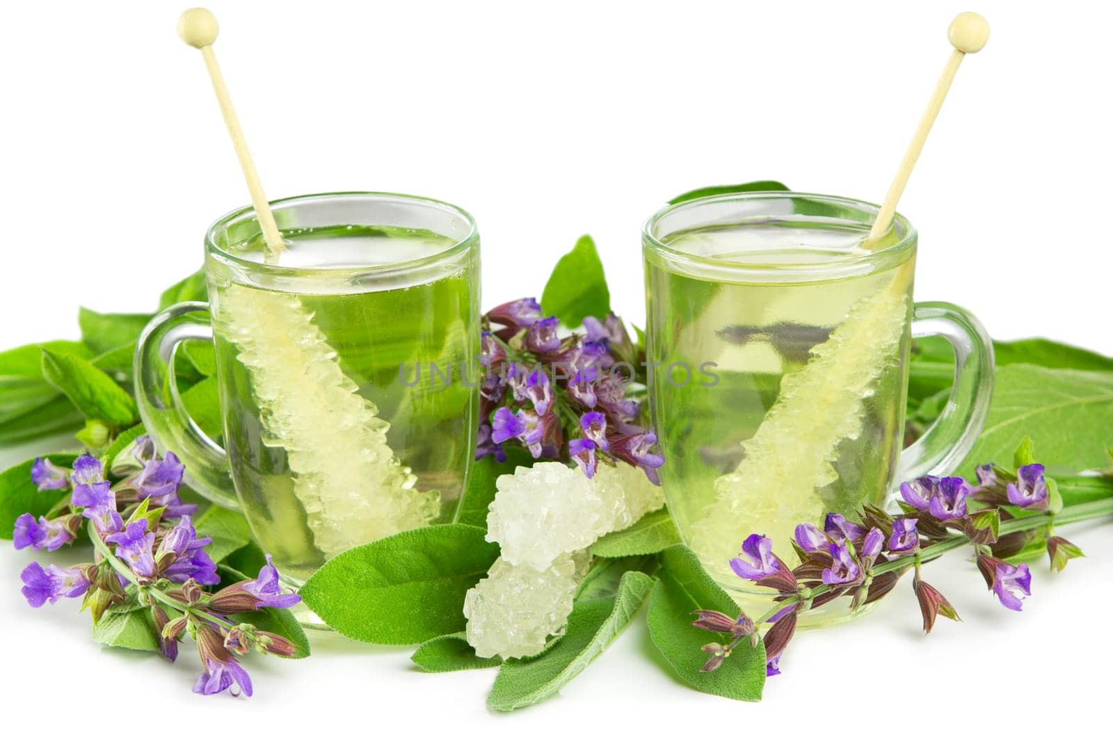 Glass mugs of ayuveda naturopathy herbal teas with sugar crystals and fresh salvia flowers on a white studio background