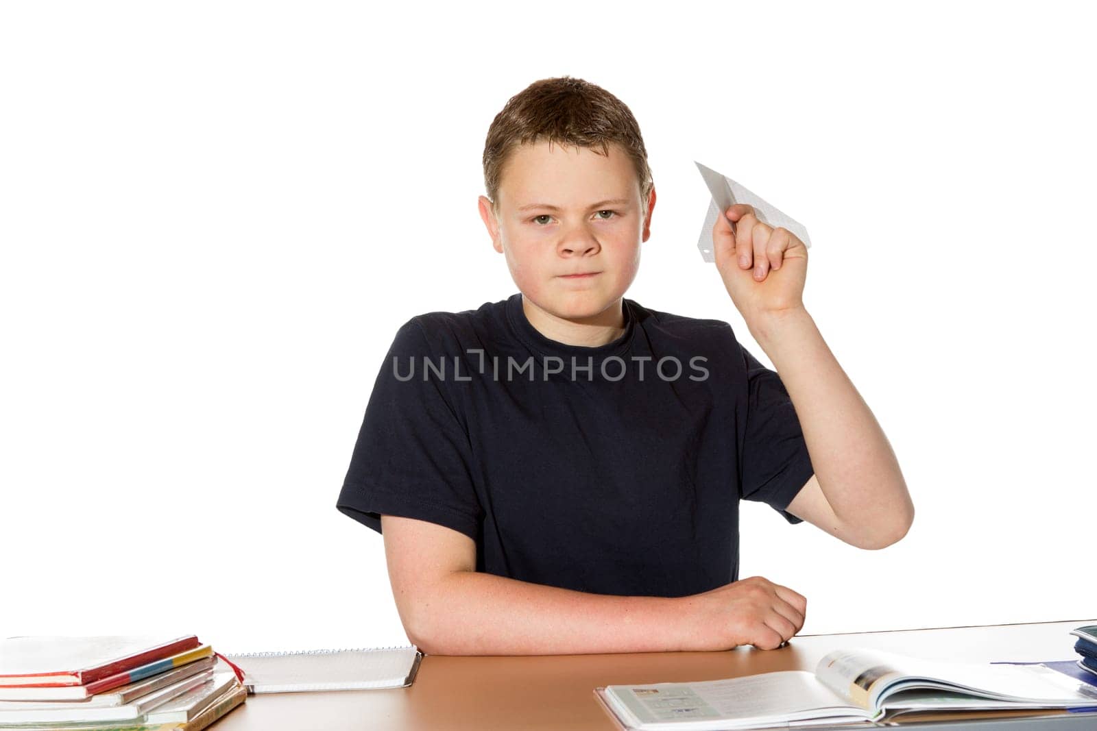 Young teenage student sitting at his desk taking aim to throw a paper plane with a message at one of his classmates