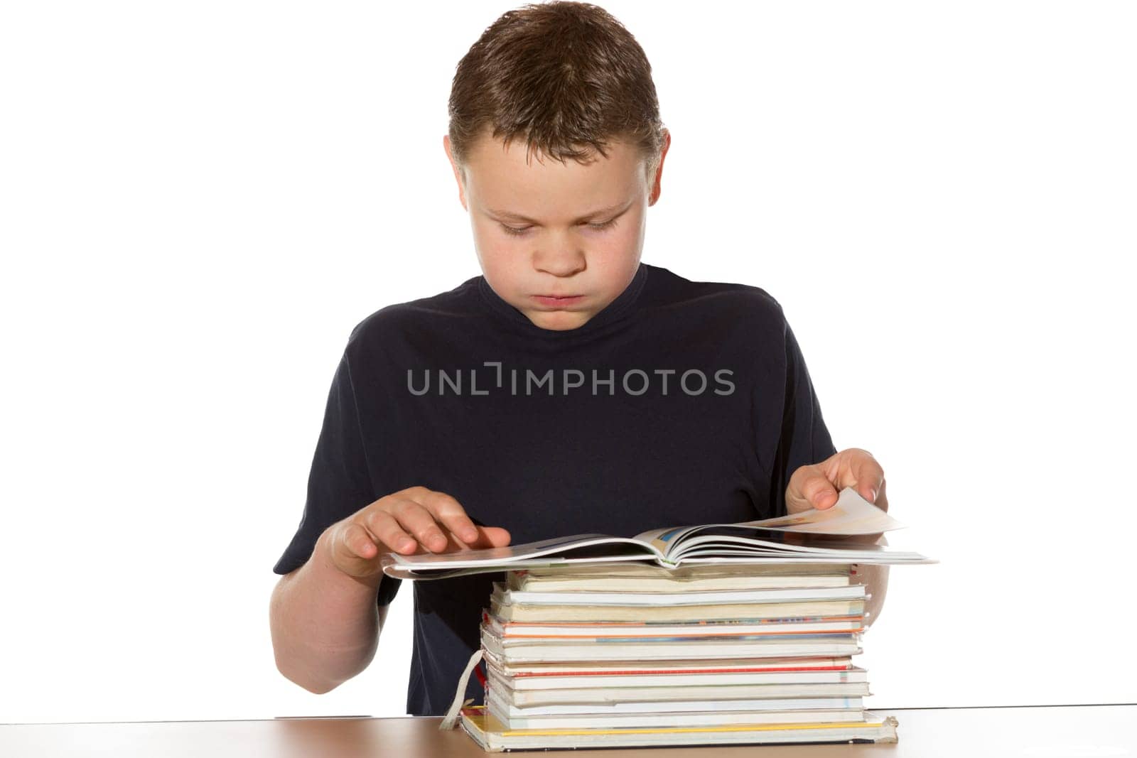 Young teenage boy or bookworm sitting at a desk reading from the top book in a pile of stacked books