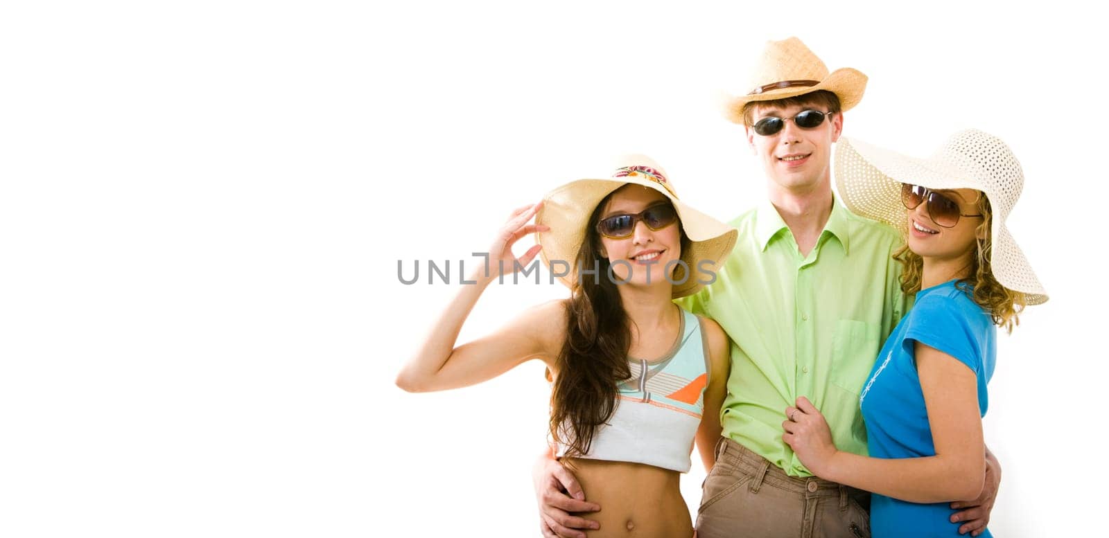 Portrait of guy wearing dark glasses standing between two fashionable girls in hats and hugging them