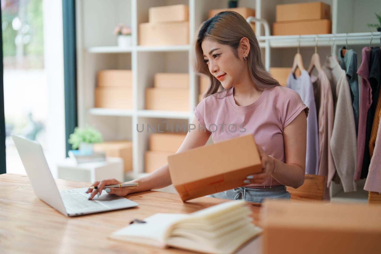 Portrait Of Asian Female Owner Of Fashion Store Checking Stock In Clothing Store With using notebook successful happy smile at small business, sme or ecommerce concepts by Manastrong