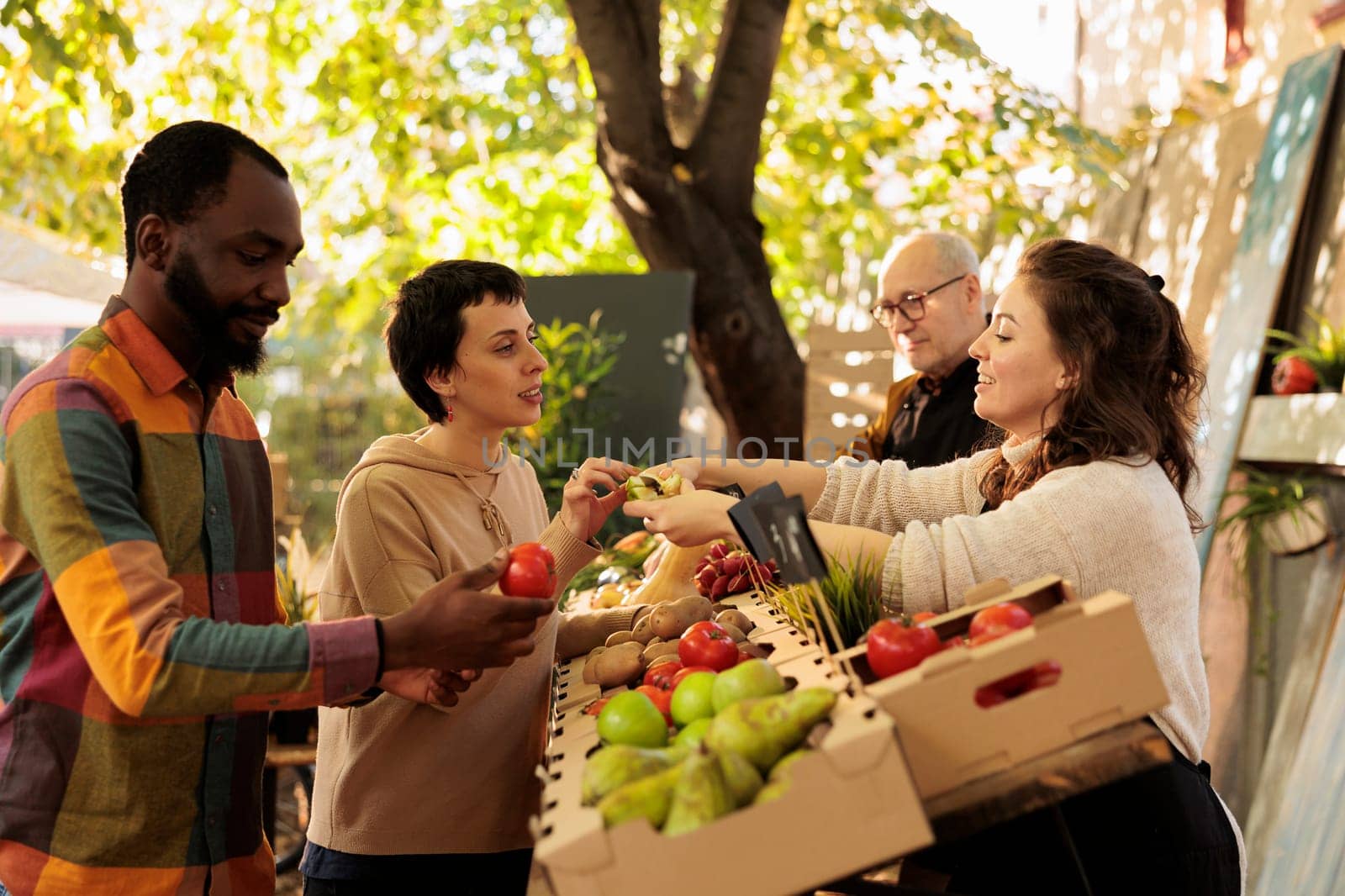 Female farmer offering samples to customers to sell homegrown fruits and vegetables at local farmers market. Young diverse couple or family tasting natural fresh produce, visiting food fair.