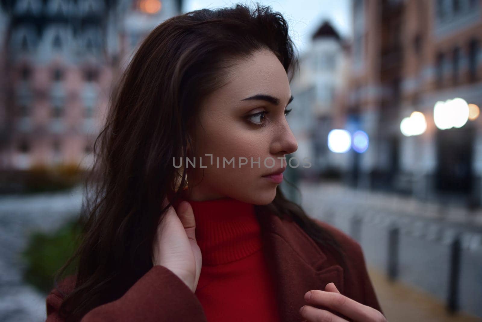 Dramatic close up portrait of young beautiful Girl looking aside against evening city background by Nickstock