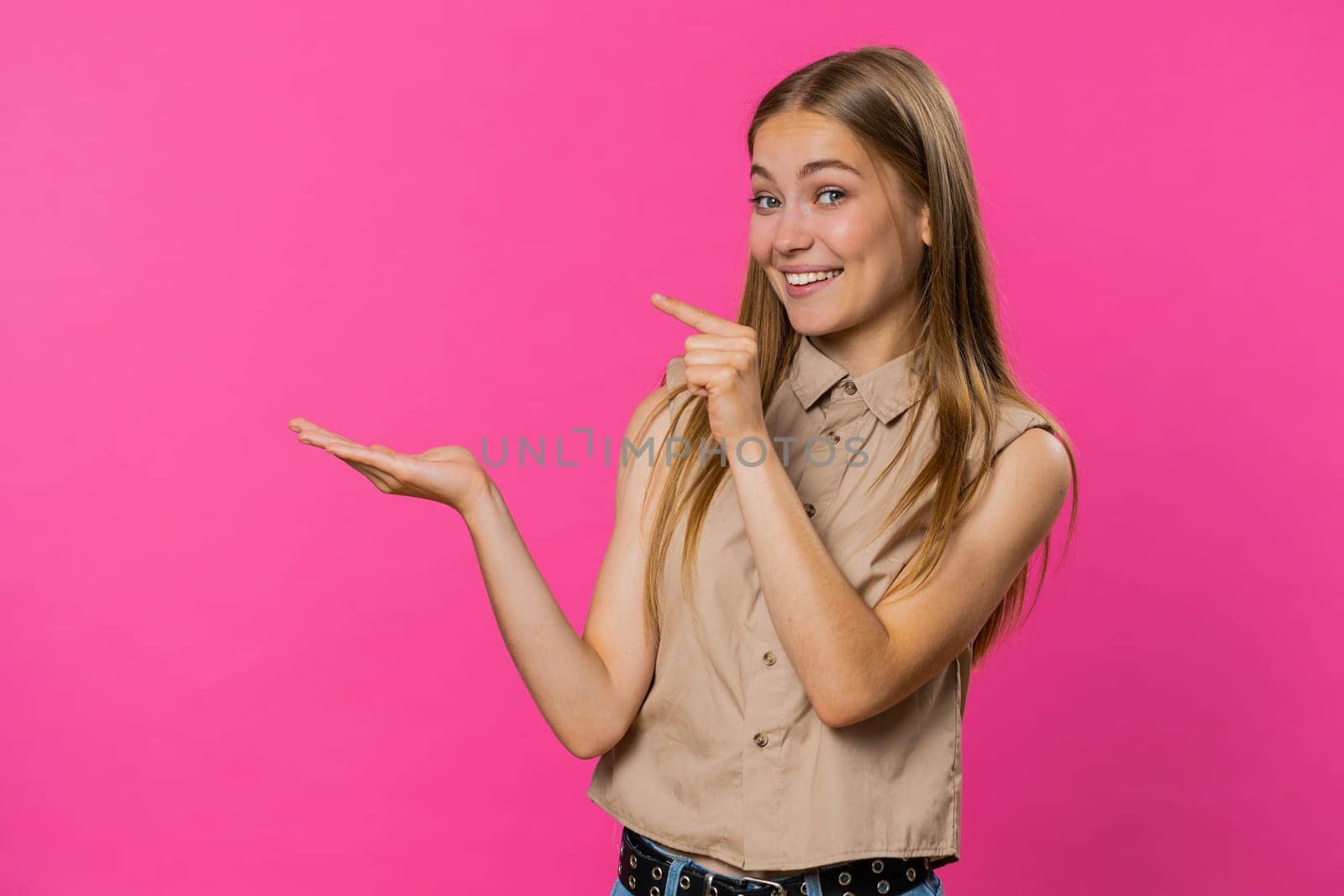Young woman showing thumbs up and pointing left empty place, advertising area for commercial text, copy space for goods promotion advertisement. Girl isolated on pink studio background. Lifestyles
