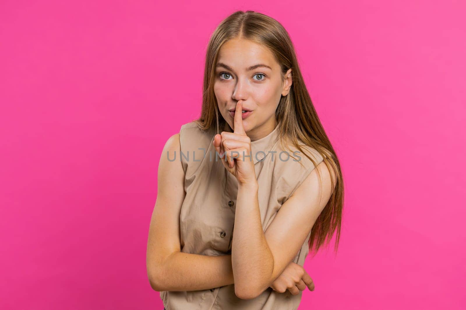 Shh be quiet please. Young woman presses index finger to lips makes silence gesture sign do not tells secret, stop gossip. Pretty attractive blonde girl isolated alone on pink studio background