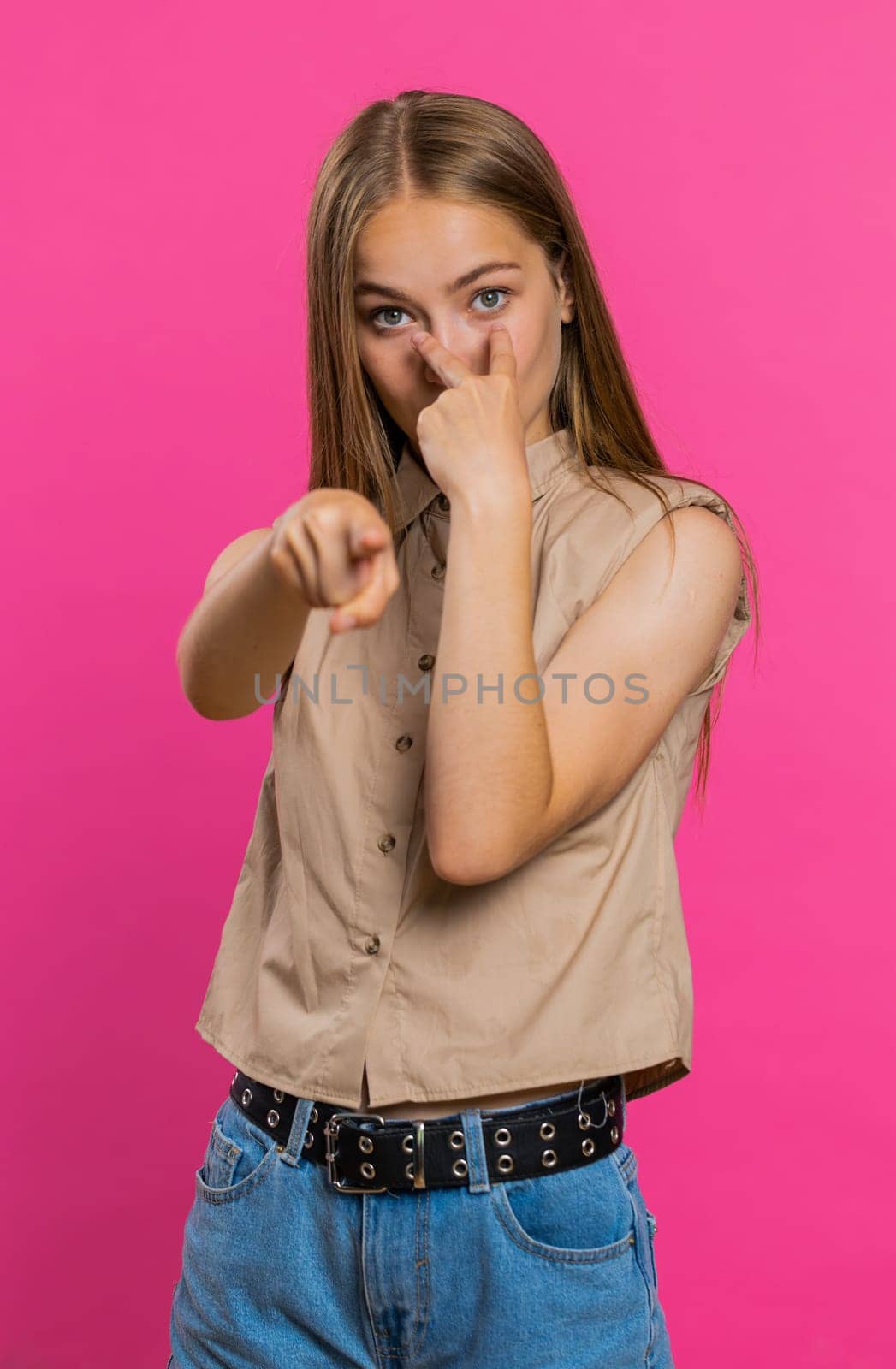 I am watching you. Young confident woman pointing at her eyes and camera, show I am watching you gesture, spying on someone. Pretty blonde adult girl isolated alone on pink studio background. Vertical