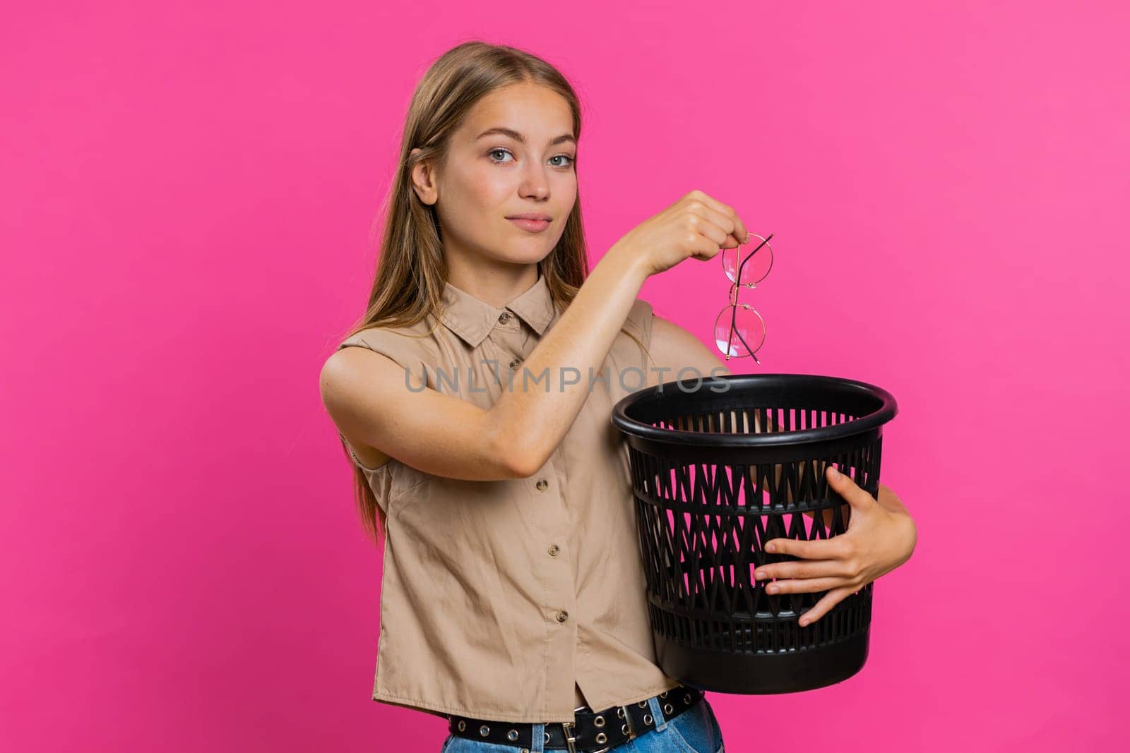 Blonde attractive woman taking off throwing out glasses into bin after medical vision laser treatment therapy surgery looking smiling at camera. Pretty girl isolated on pink studio background