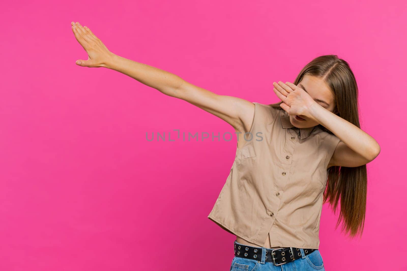 Trendy cheerful positive young woman having fun dancing and moving to rhythm, dabbing raising hands, making dub dance winner gesture. Happy girl isolated alone on pink studio background. Lifestyles