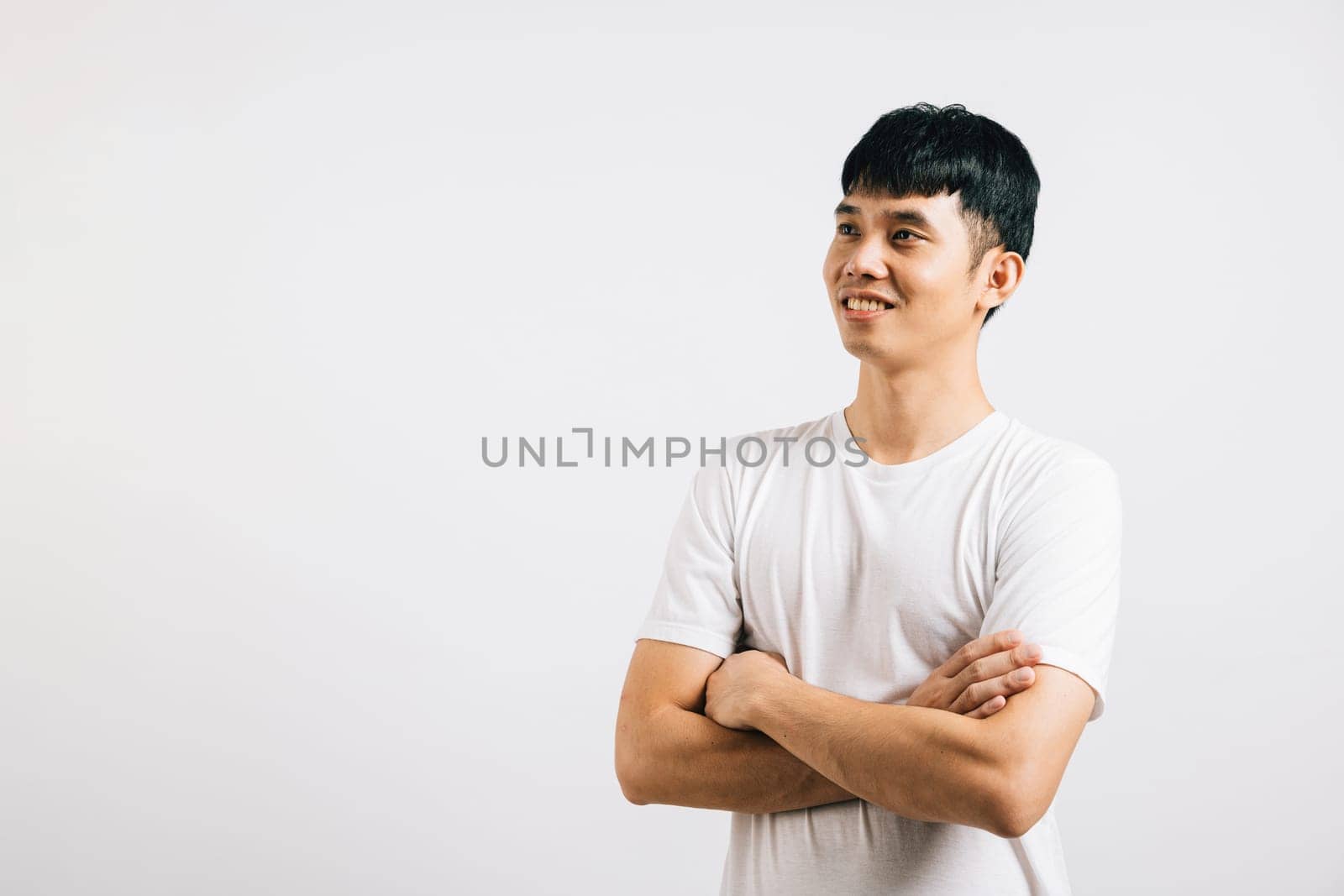 Confident Asian man showcases success with crossed arms and a beaming smile. Studio portrait isolated on white background, radiating positivity and happiness.