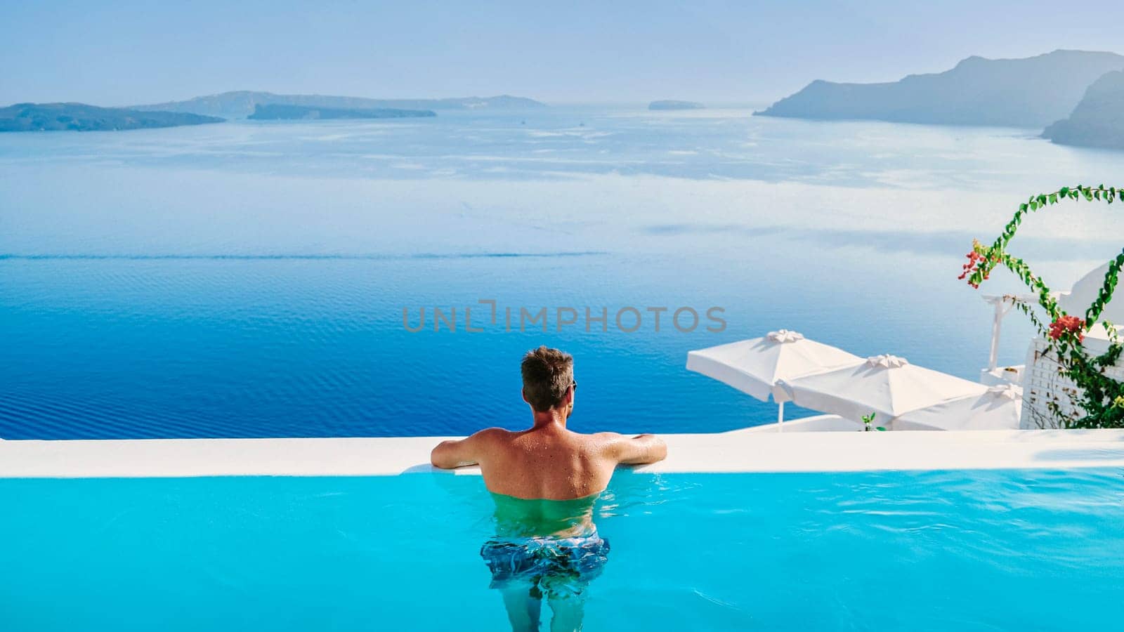 Young men in swim short relaxing in the pool looking out over the caldera of Santorini Greece by fokkebok