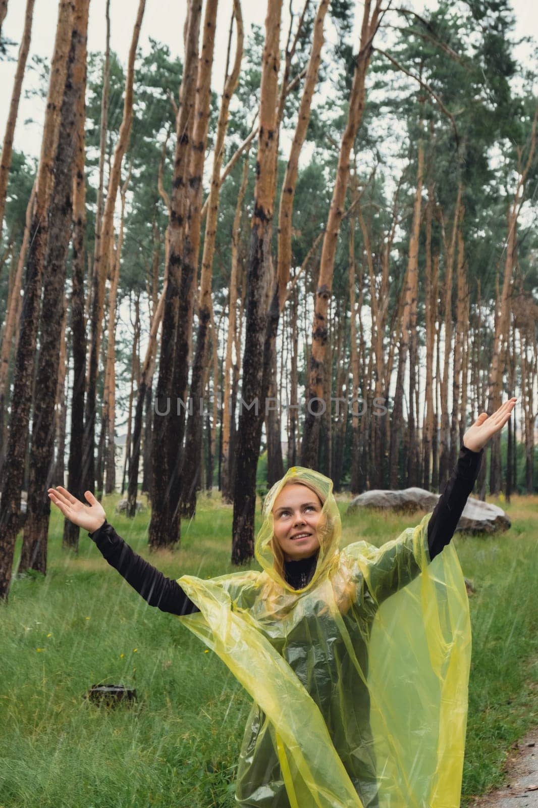 Smiling woman in yellow raincoat walking in autumn forest enjoying rainy weather outdoors. Female tourist discover park in rainy season. Closeness to nature. Mental healing fulfillment clean air