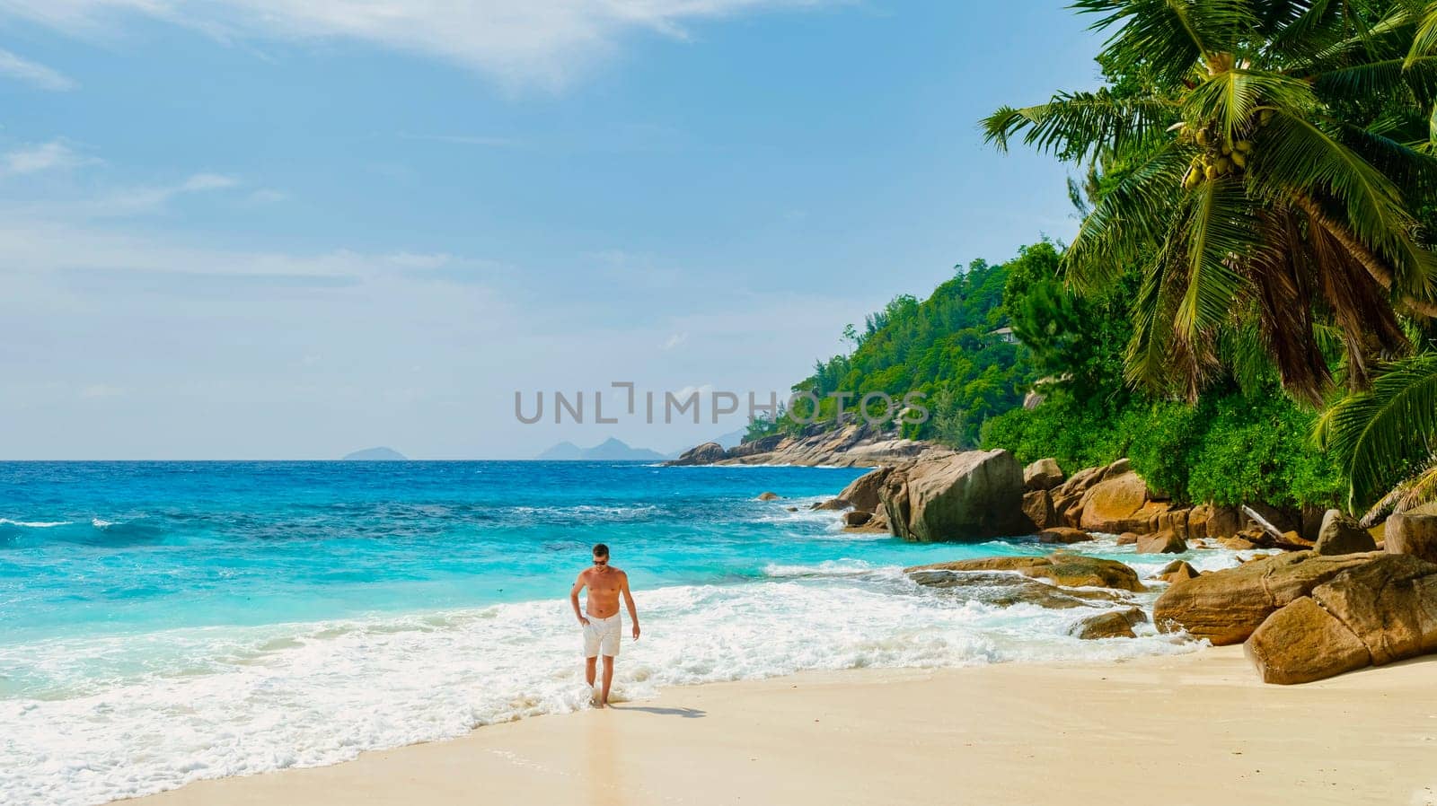 Young men in swimshort on a white tropical beach with palm trees Petite Anse beach Mahe Seychelles by fokkebok