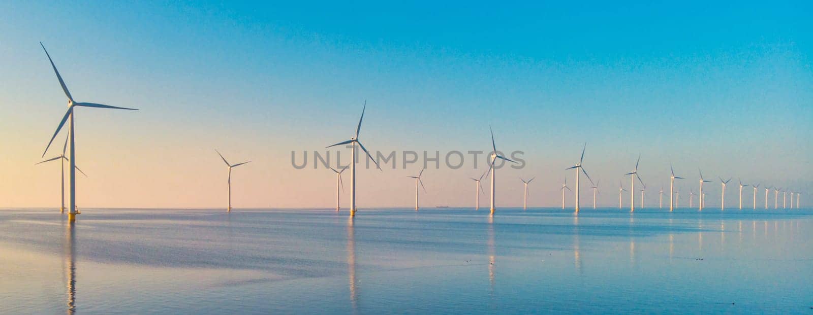 Windmill turbines at sea, drone aerial view from above at a huge windmill park in the Netherlands. Green Energy Transformation in the Netherlands Europe, windmills at sunset