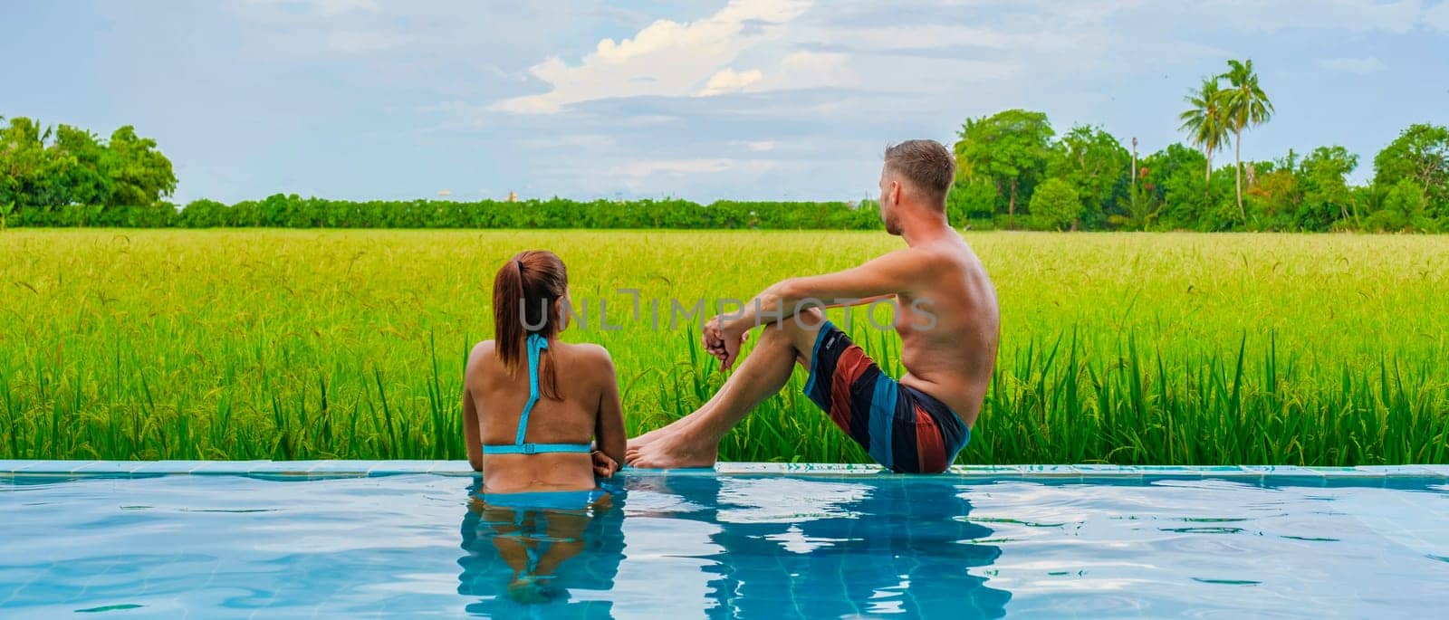 a couple of men and women in front of a Bamboo hut homestay farm, with Green rice paddy fields in Central Thailand with a small plunge pool