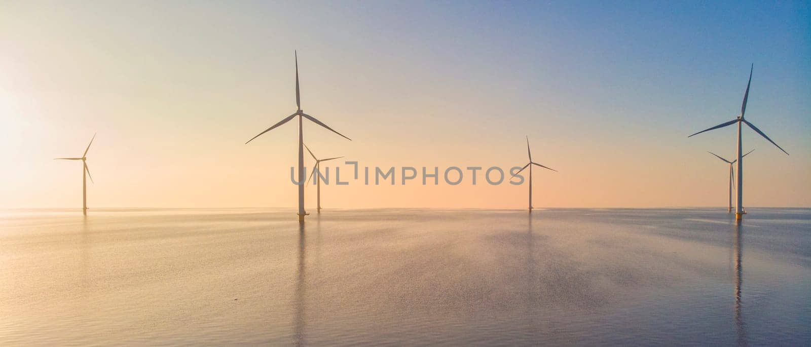 Windmill park in the ocean at sunset, drone aerial view of windmill turbines generating green energy, windmills isolated at sea in the Netherlands.
