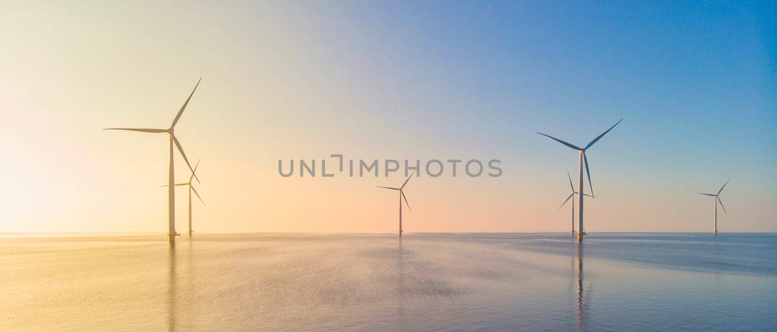 Windmill park in the ocean, drone aerial view of windmill turbines generating green energy, windmills isolated at sea in the Netherlands at sunset