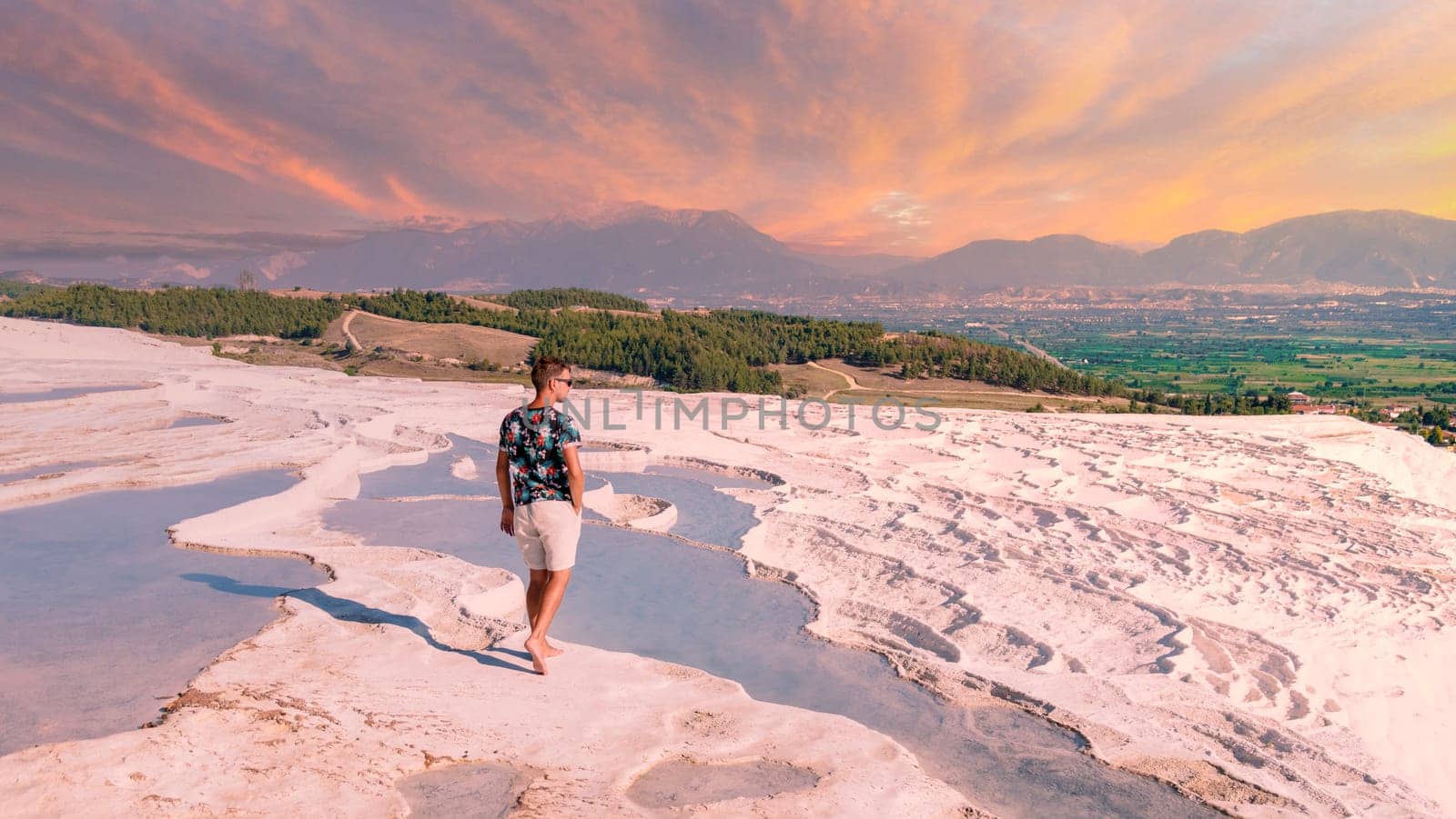 Natural travertine pools and terraces in Pamukkale. Cotton castle in southwestern Turkey, men watching the sunset at natural pool Pamukkale Thermal baths in Turkey