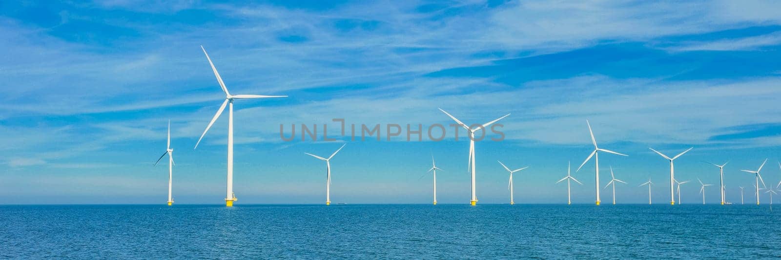 Drone view at windmill turbines, Windmill park with clouds and a blue sky, windmill park in the ocean aerial view with wind turbine Flevoland Netherlands