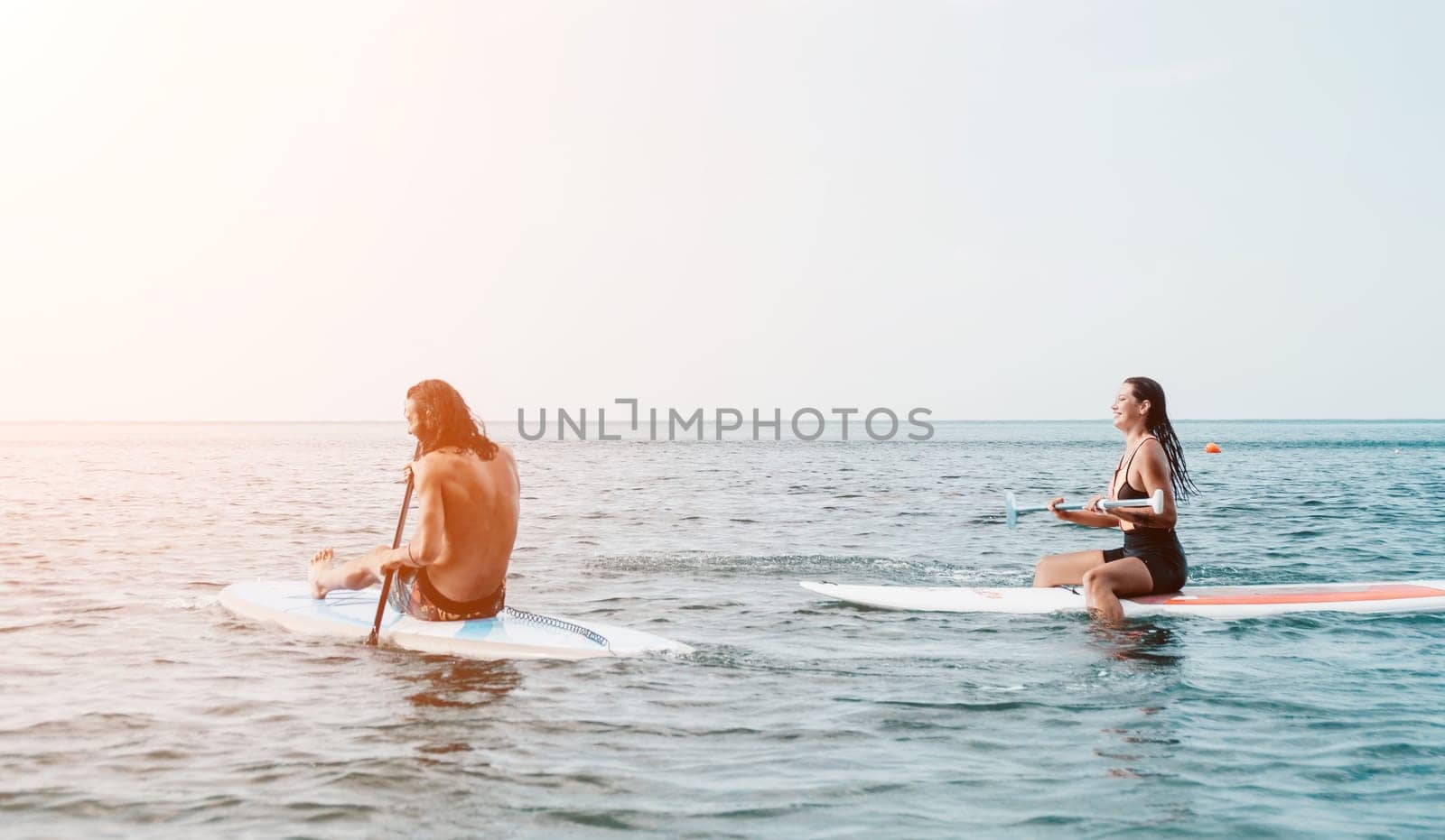Woman man sup yoga. Happy young sporty couple practising yoga pilates on paddle sup surfboard. Female stretching doing workout on sea water. Modern family outdoor summer sport activity. by panophotograph