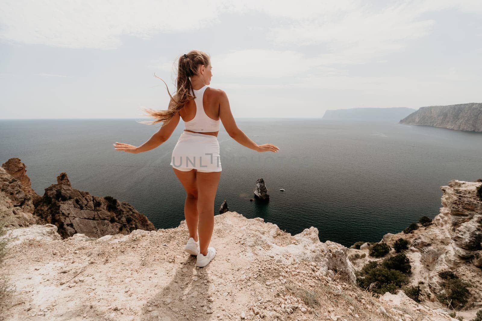 Woman travel sea. Happy tourist in hat enjoy taking picture outdoors for memories. Woman traveler posing on the beach at sea surrounded by volcanic mountains, sharing travel adventure journey