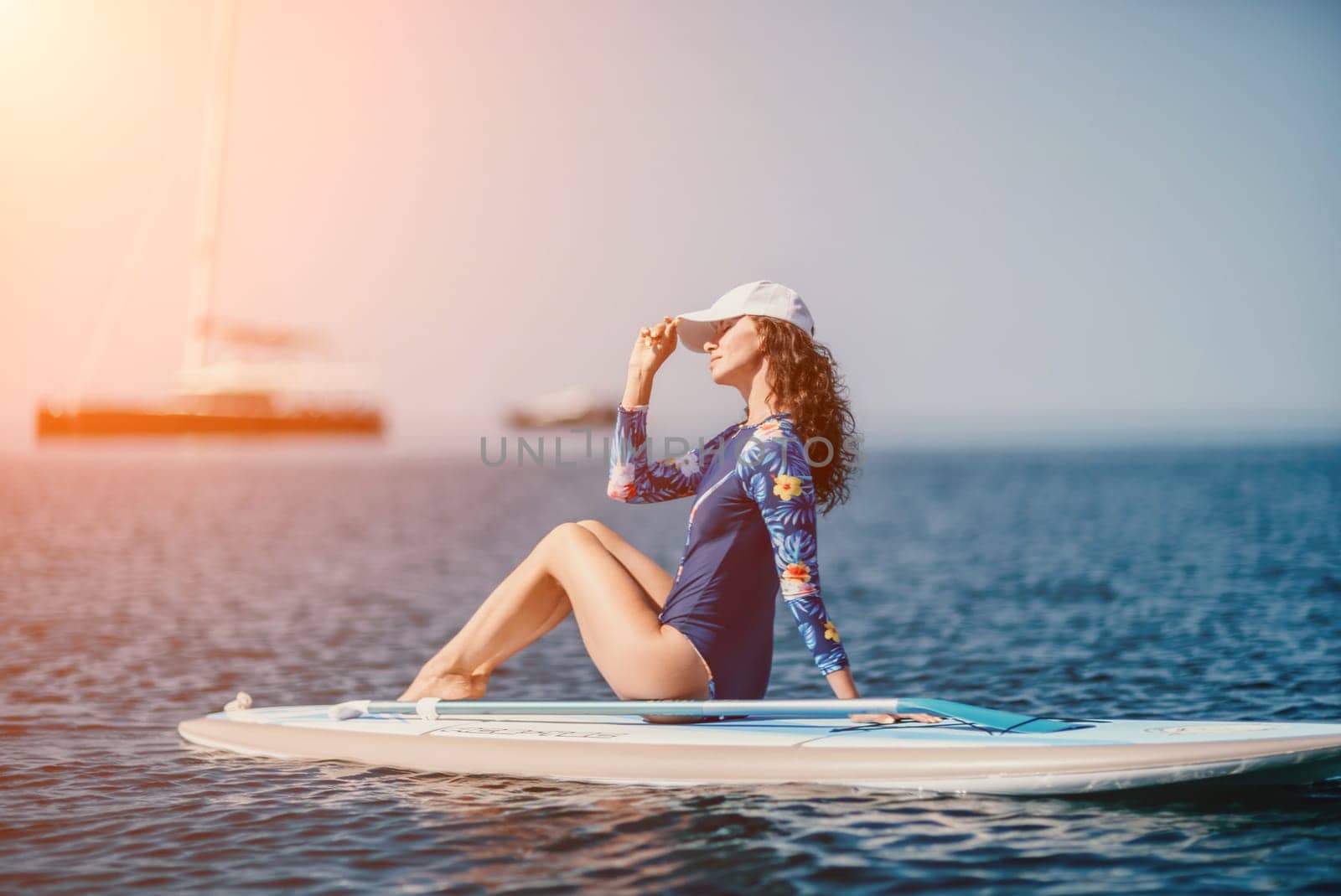 Woman sup yoga. Middle age sporty woman practising yoga pilates on paddle sup surfboard. Female stretching doing workout on sea water. Modern individual female hipster outdoor summer sport activity. by panophotograph