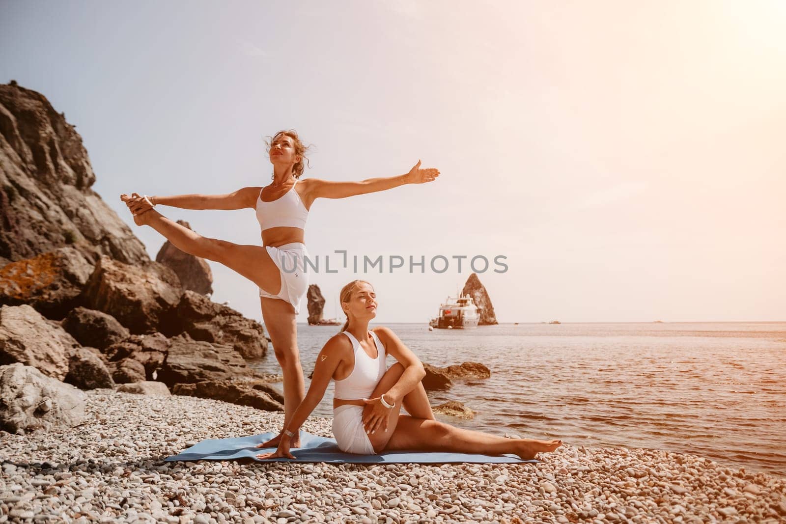 Woman sea yoga. Two happy women practicing yoga on the beach with ocean and rock mountains. Motivation and inspirational fit and exercising. Healthy lifestyle outdoors in nature, fitness concept. by panophotograph