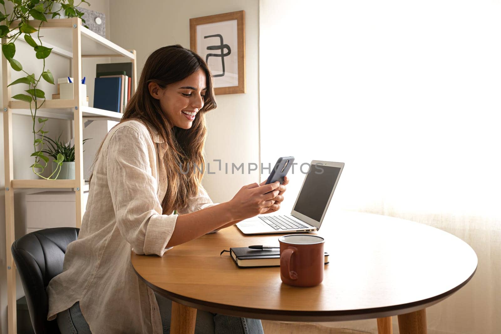 Happy young woman using mobile phone working at home. Copy space. Working from home concept.