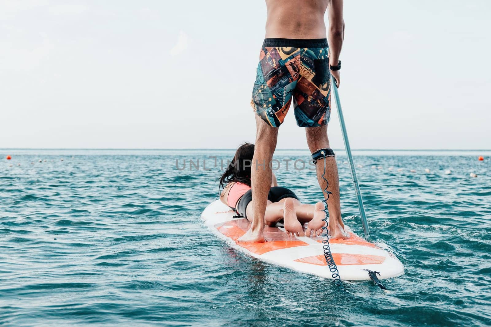 Sea woman and man on sup. Silhouette of happy young woman and man, surfing on SUP board, confident paddling through water surface. Idyllic sunset. Active lifestyle at sea or river