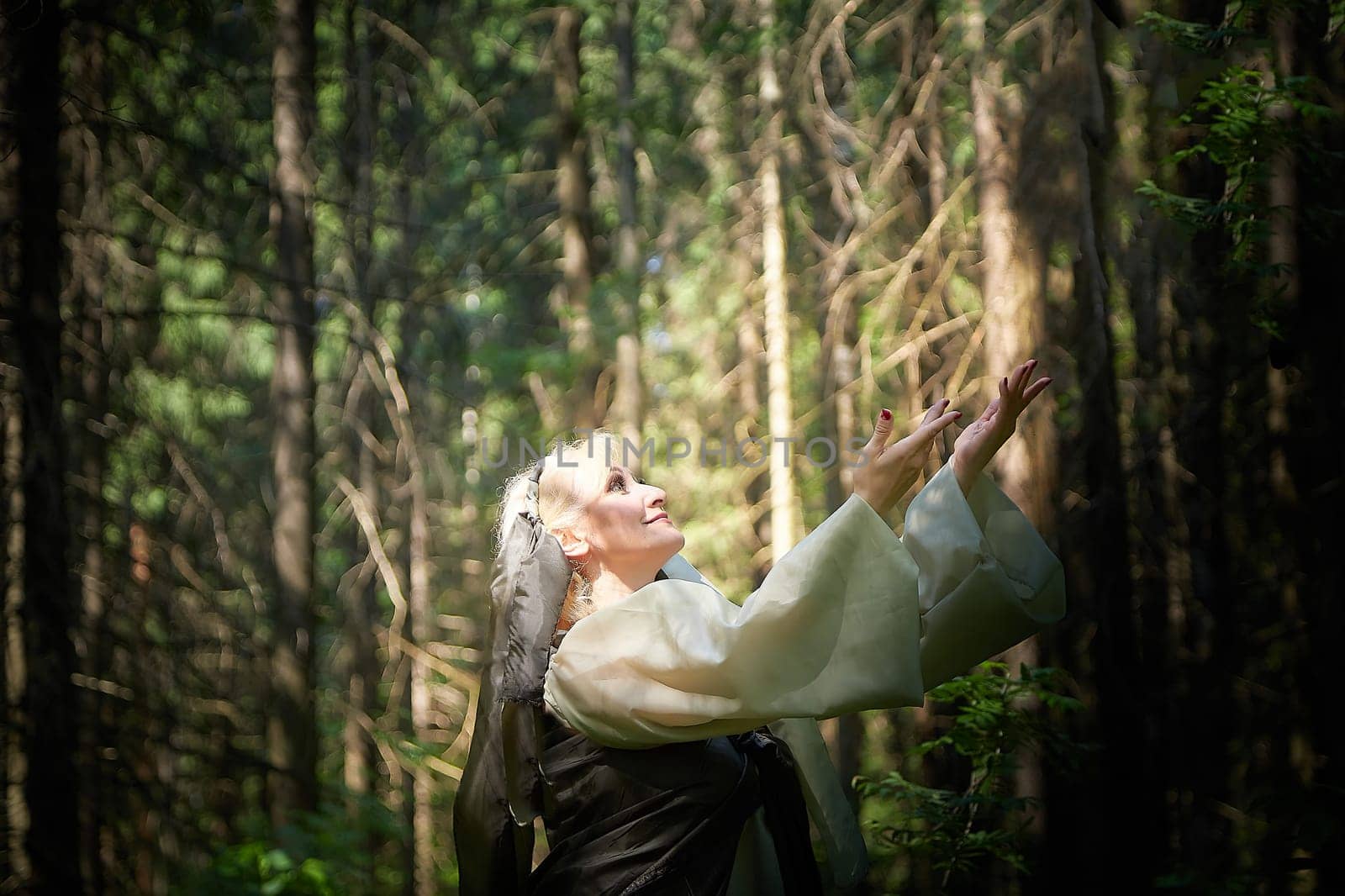 Adult mature woman 40-60 in a green long fairy dress in forest. Photo shoot in style of dryad and queen of nature. Fairy in beautiful green summer forest. Concept of caring for nature