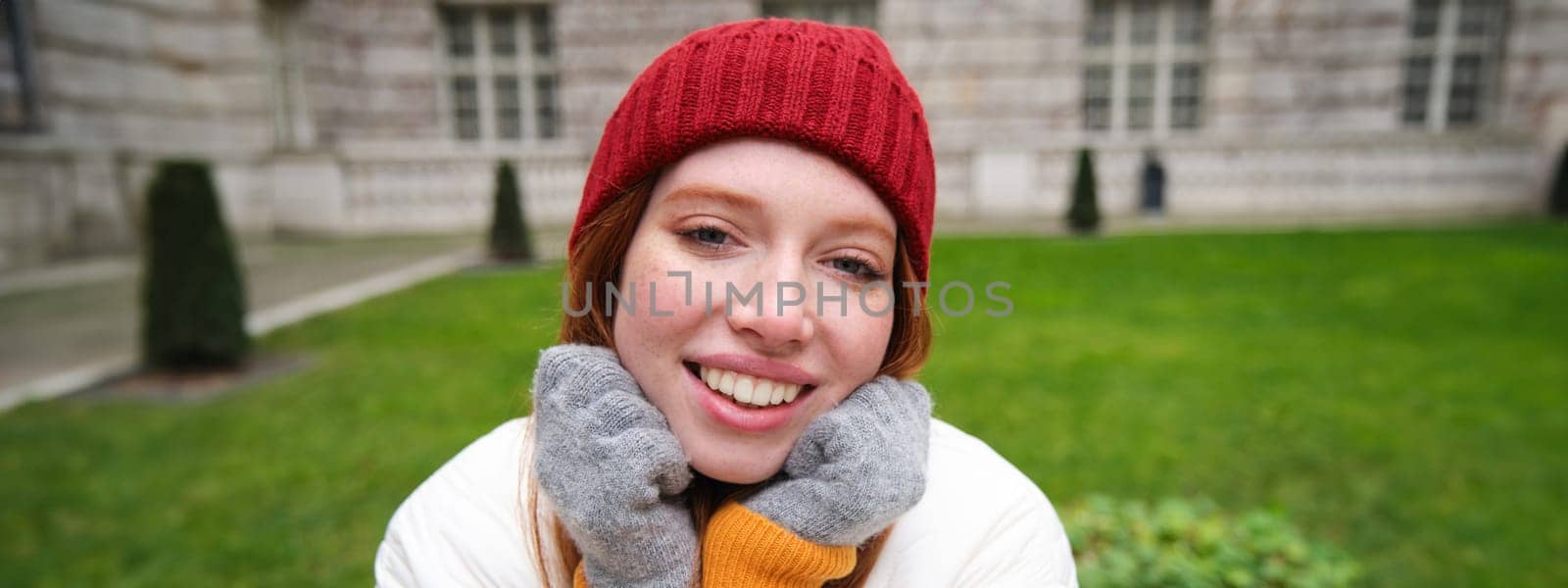 Cute girl student in red hat, warm gloves, sits in park, smiles and looks happy. by Benzoix