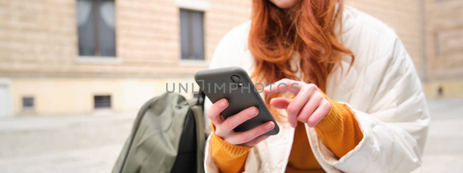 Close up of female hands typing on mobile phone, using smartphone app. GIrl with telephone types, sits outdoors and uses map.