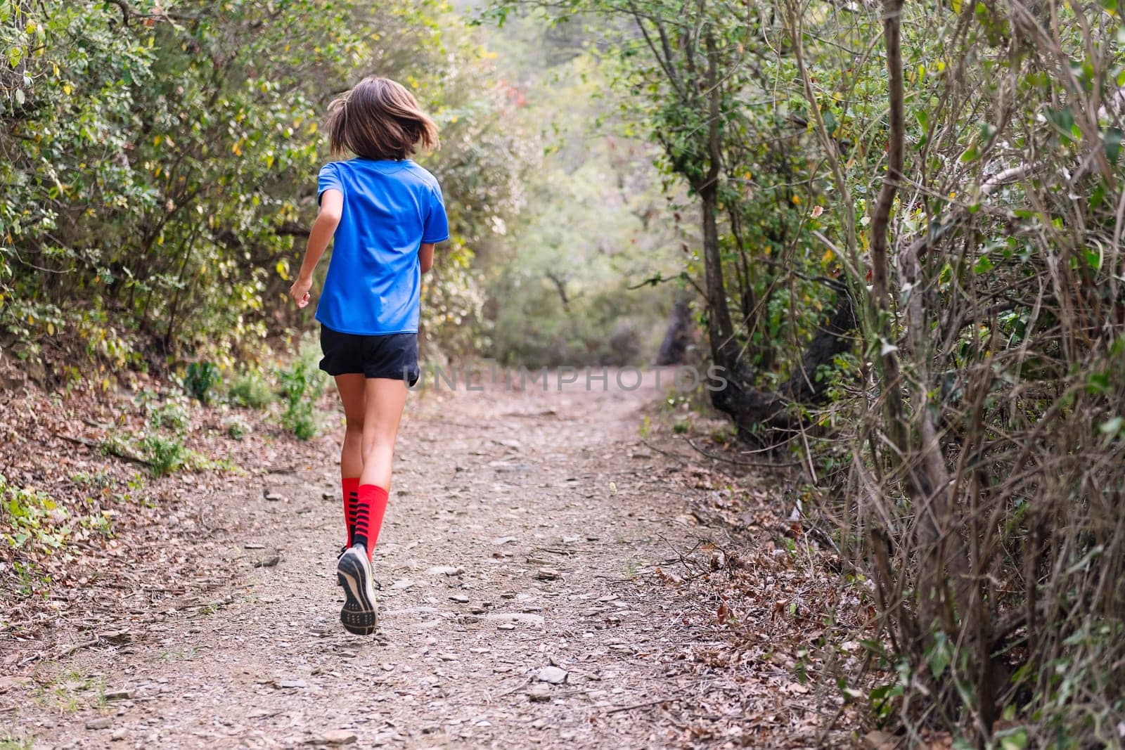 rear view of a kid practicing trail running in the forest, concept of sport in nature and healthy lifestyle for children, copy space for text