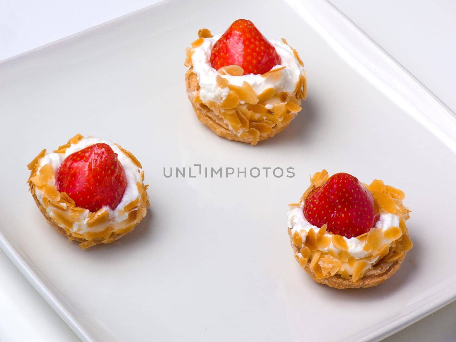 Three tasty strawberry tarts on a sqare plate, closeup