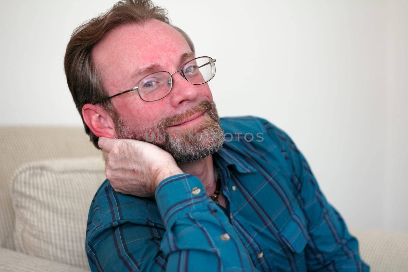 Middle aged man leaning the side of his face on his hand looking at the viewer in a relaxed way with a slight smile.