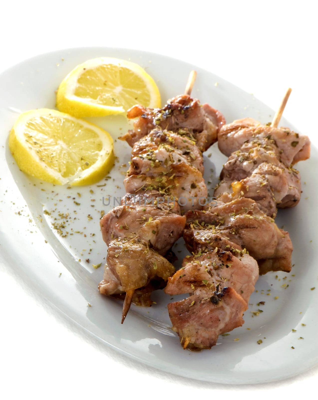 Two greek souvlaki or kalamaki in a plate with lemons, isolated on white background