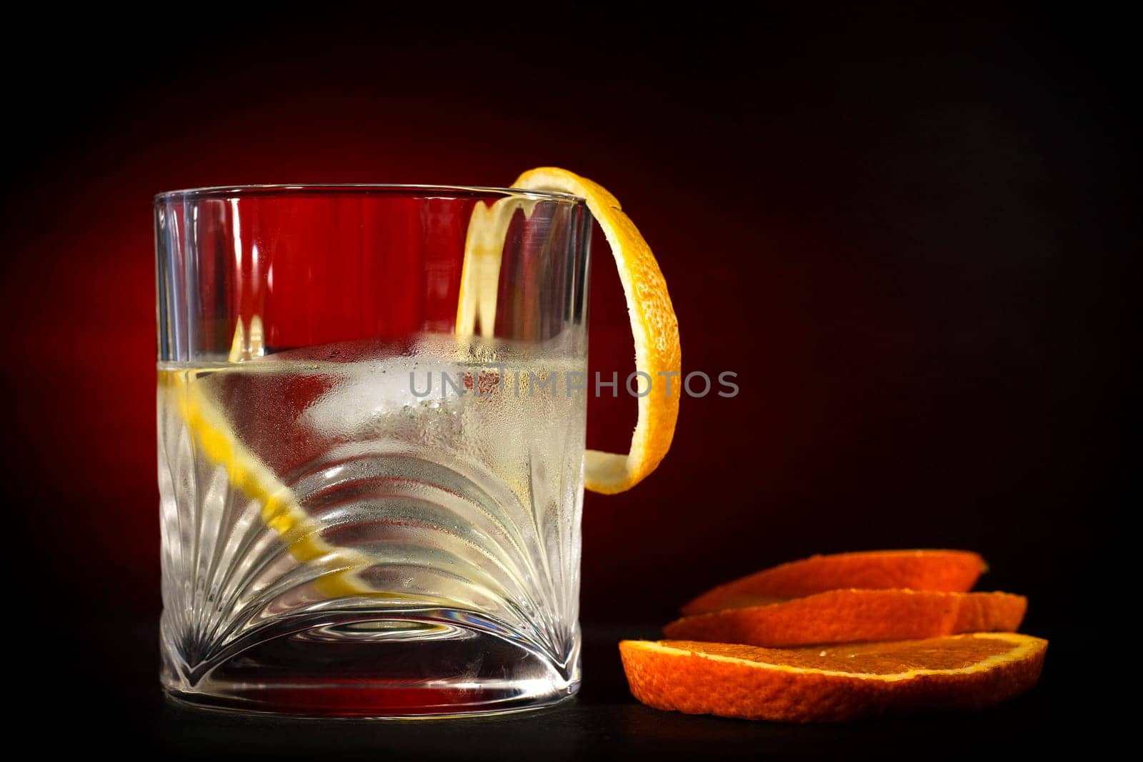 Cold vodka in a glass, with decor oranges and lemon, in black red background, part of art beverage background