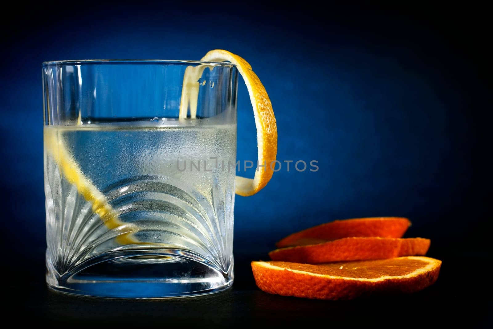 Cold vodka in a glass, with decor oranges and lemon, in black blue background, part of art beverage background
