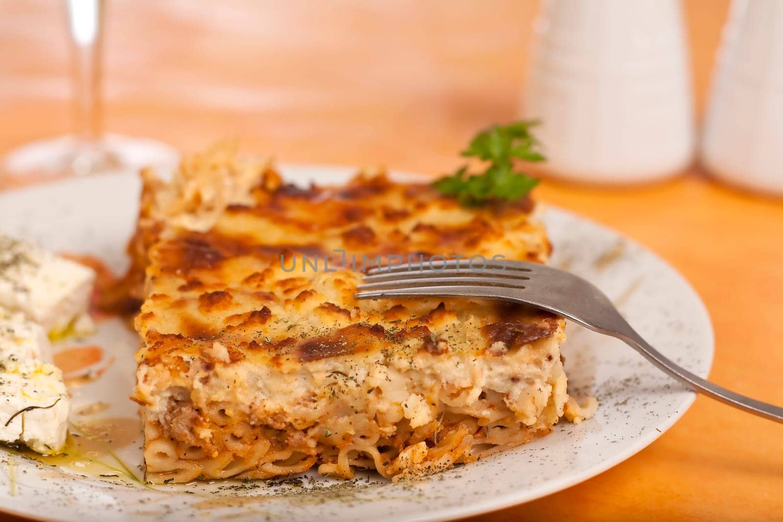 Pastitsio greek food on a table, wine alcohol drink salt, feta cheese and pepper