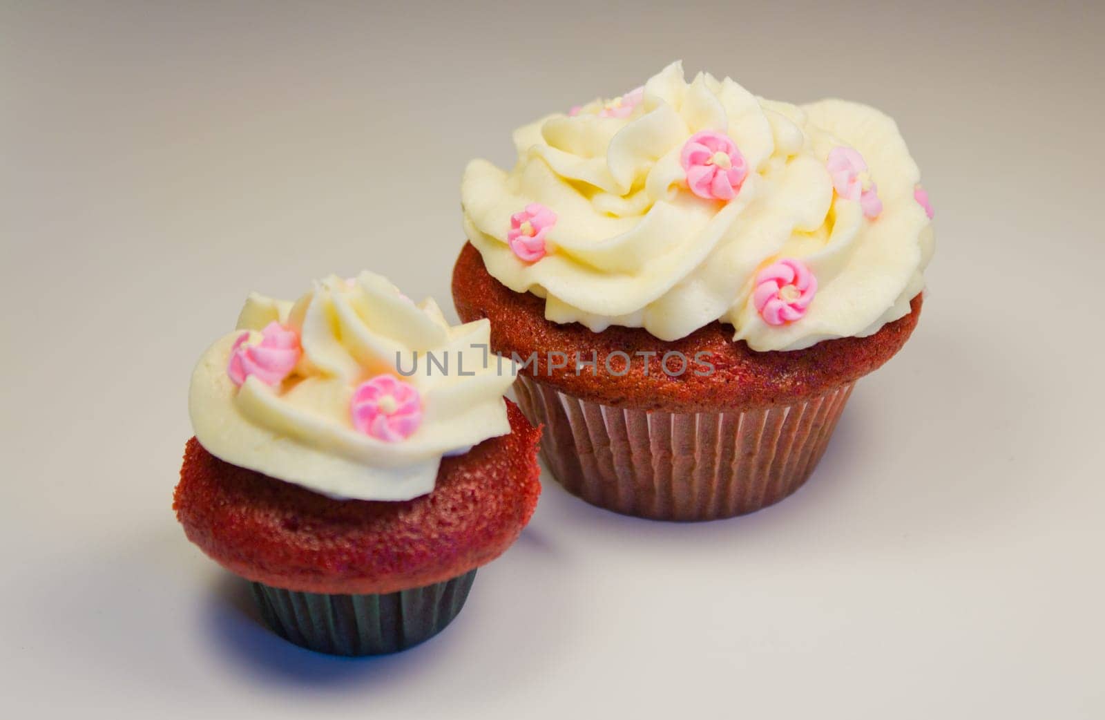 Red velvet cupcakes with buttercream icing with flower decorations isolated on white.