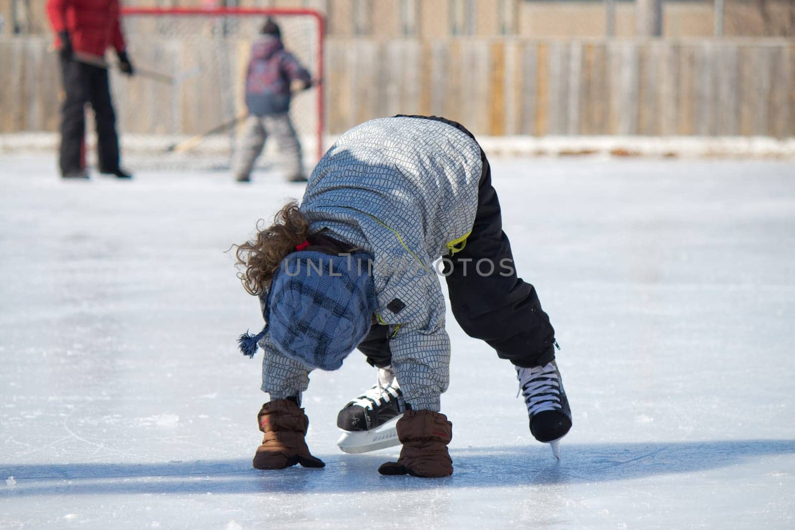 Child playing and skating at the outdoor skating rink in winter.