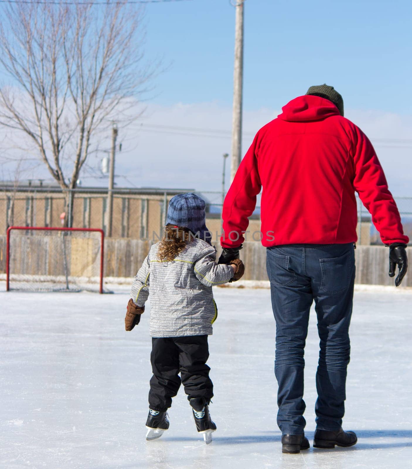 Father teaching daughter how to ice skate at an outdoor skating rink in winter.