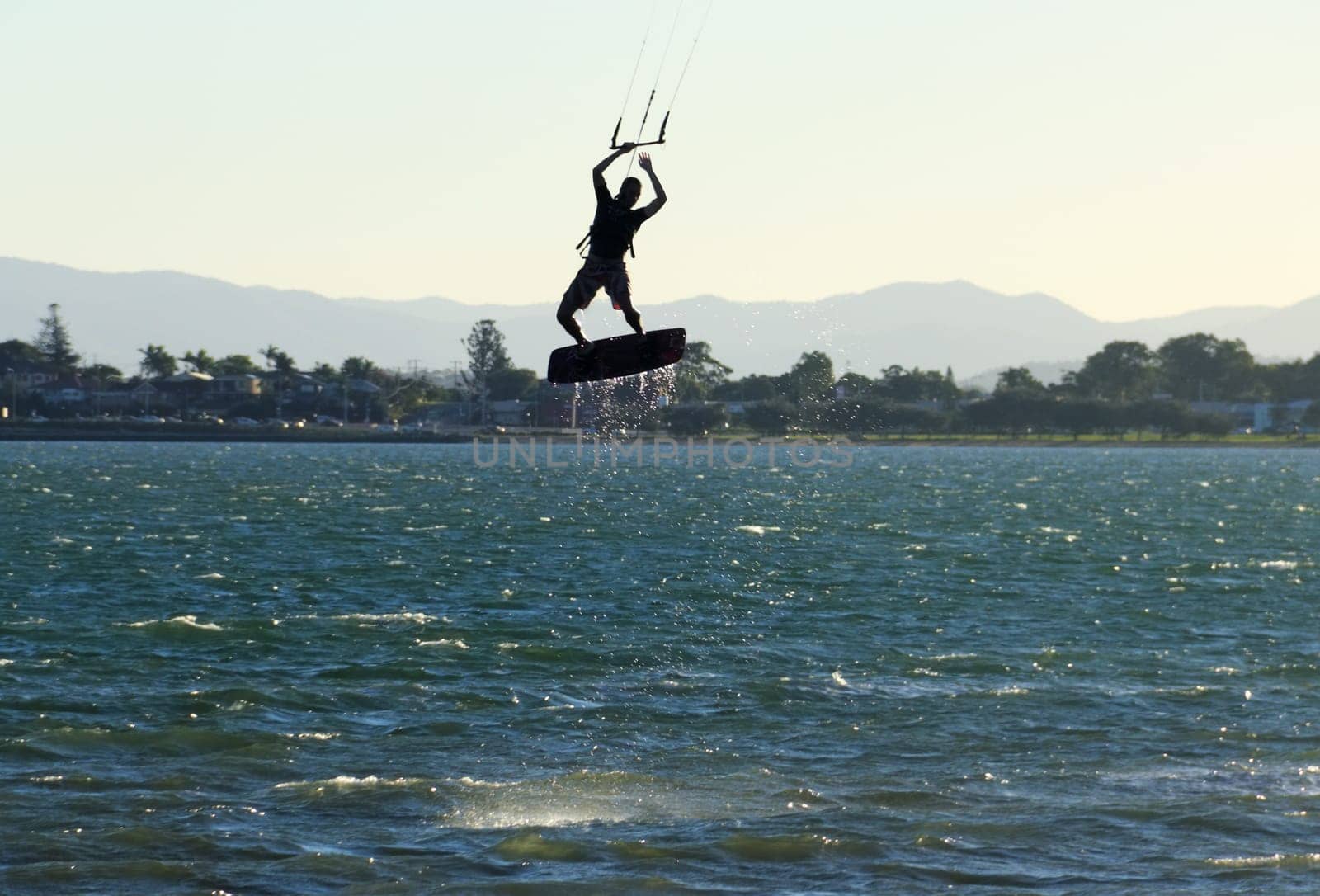 Kite surfer airborne above the water at sunset.