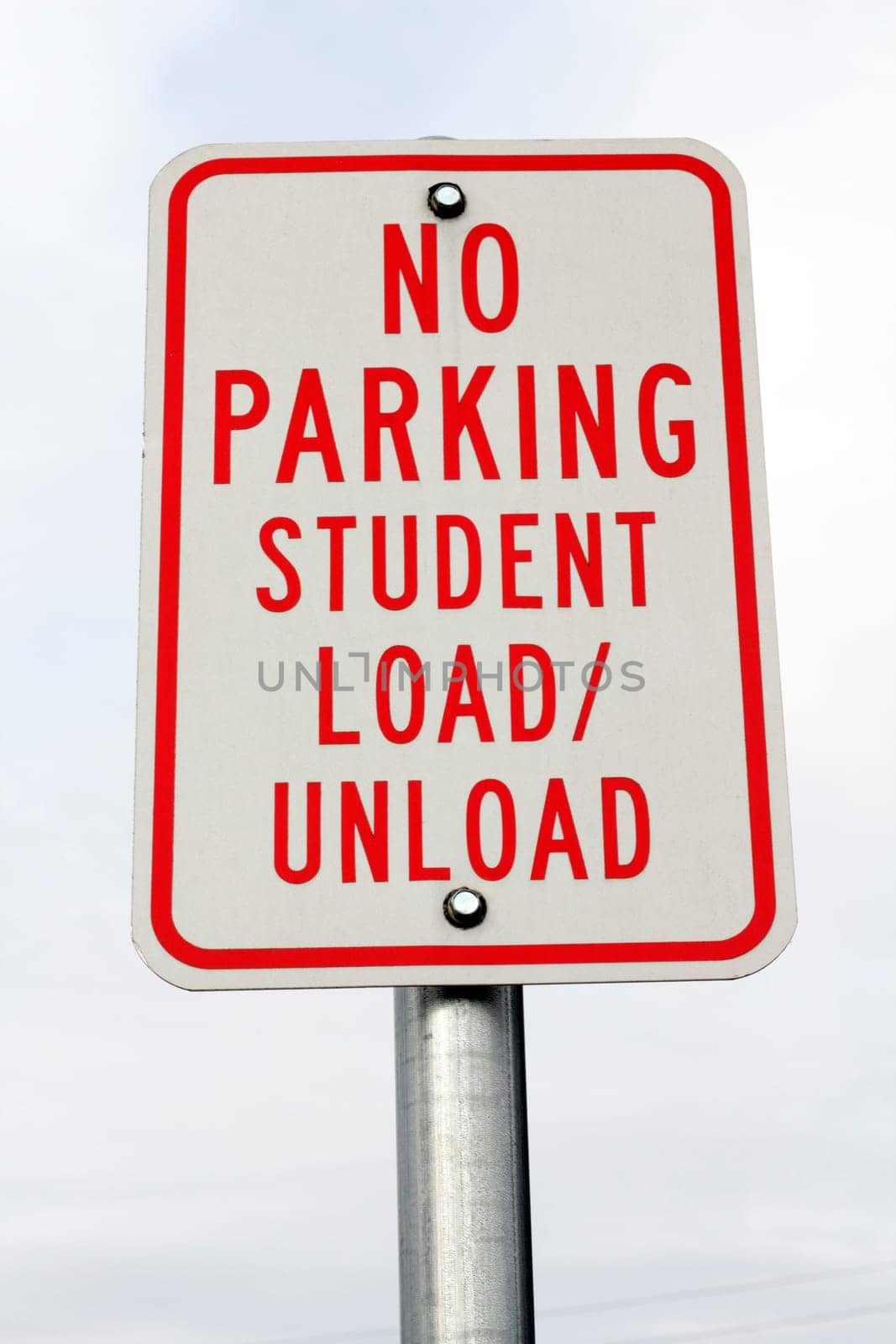 Red and white metal sign at a public school that reads in all capital letters, no parking student load / unload.