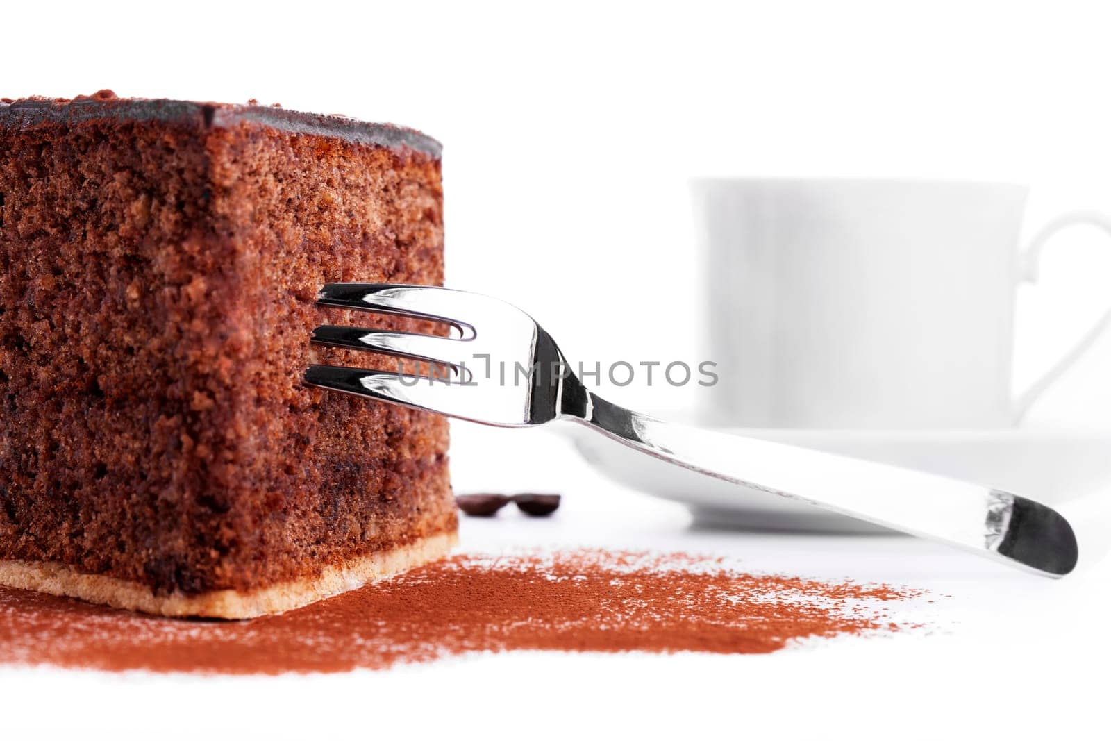 Chocolate cake with fork in front of a cup of coffee on a white background