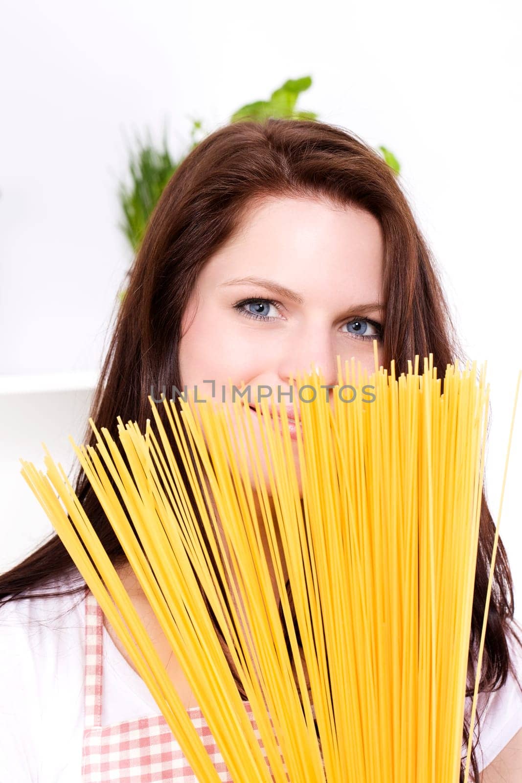 Smiling young woman hiding behind spaghetti