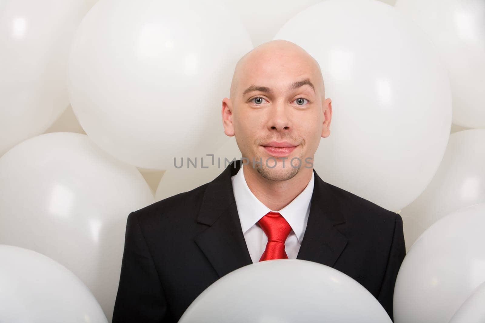 Handsome businessman surrounded by many balloons looking at camera with smile