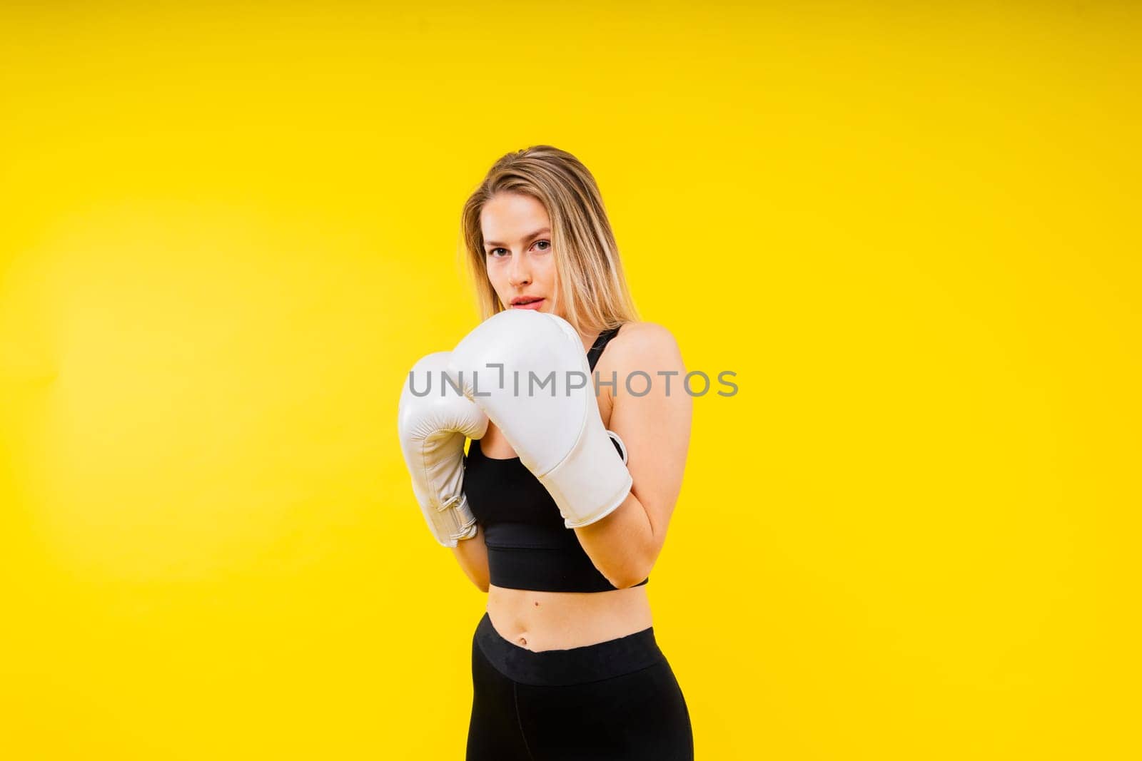 Woman boxer in gloves training on a yellow and dark studio background